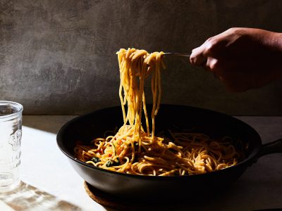 A vertical shot of a person getting some spaghetti from a black pot on a white table