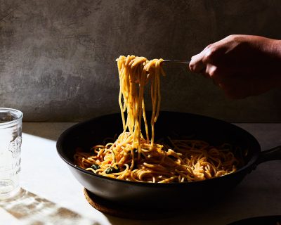 A vertical shot of a person getting some spaghetti from a black pot on a white table